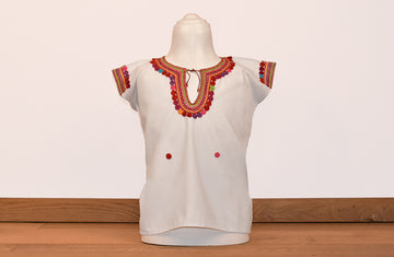 Blusa blanca para niña con bolitas y bordados de color en cuello y mangas.