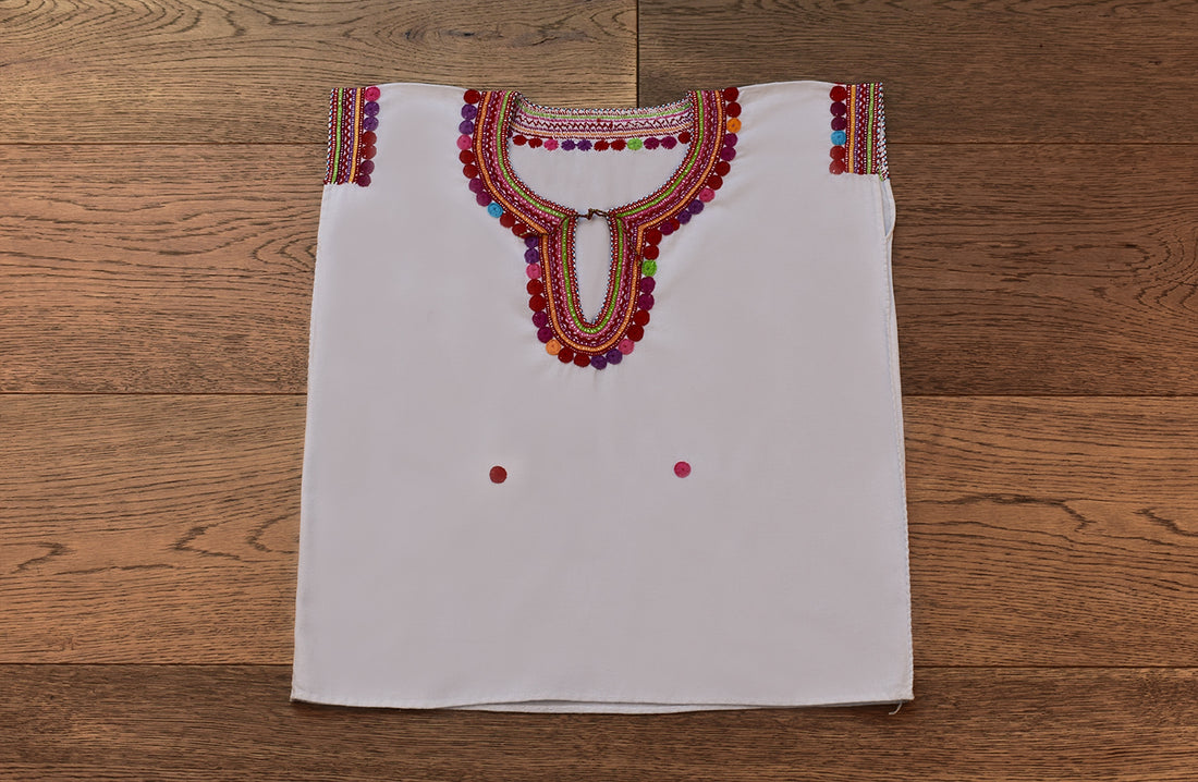 Blusa blanca para niña con bolitas y bordados de color en cuello y mangas.