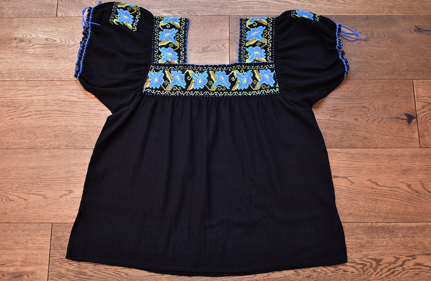 Blusa negra con punto de cruz azul en cuello y mangas.