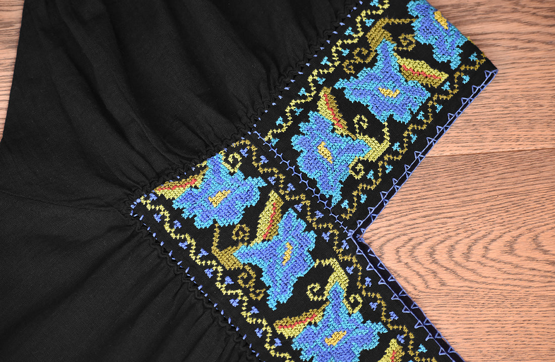 Blusa negra con punto de cruz azul en cuello y mangas.